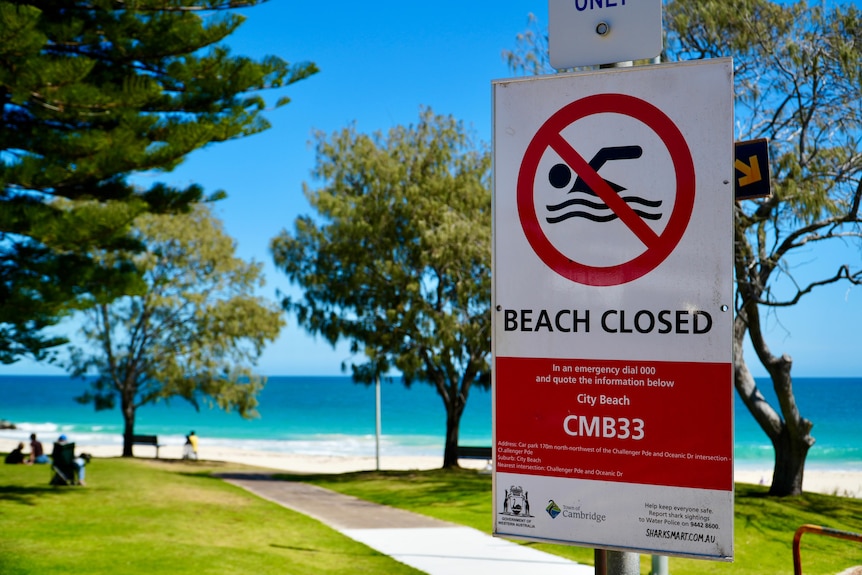 A beach closed sign on the grass at a City Beach on a sunny day