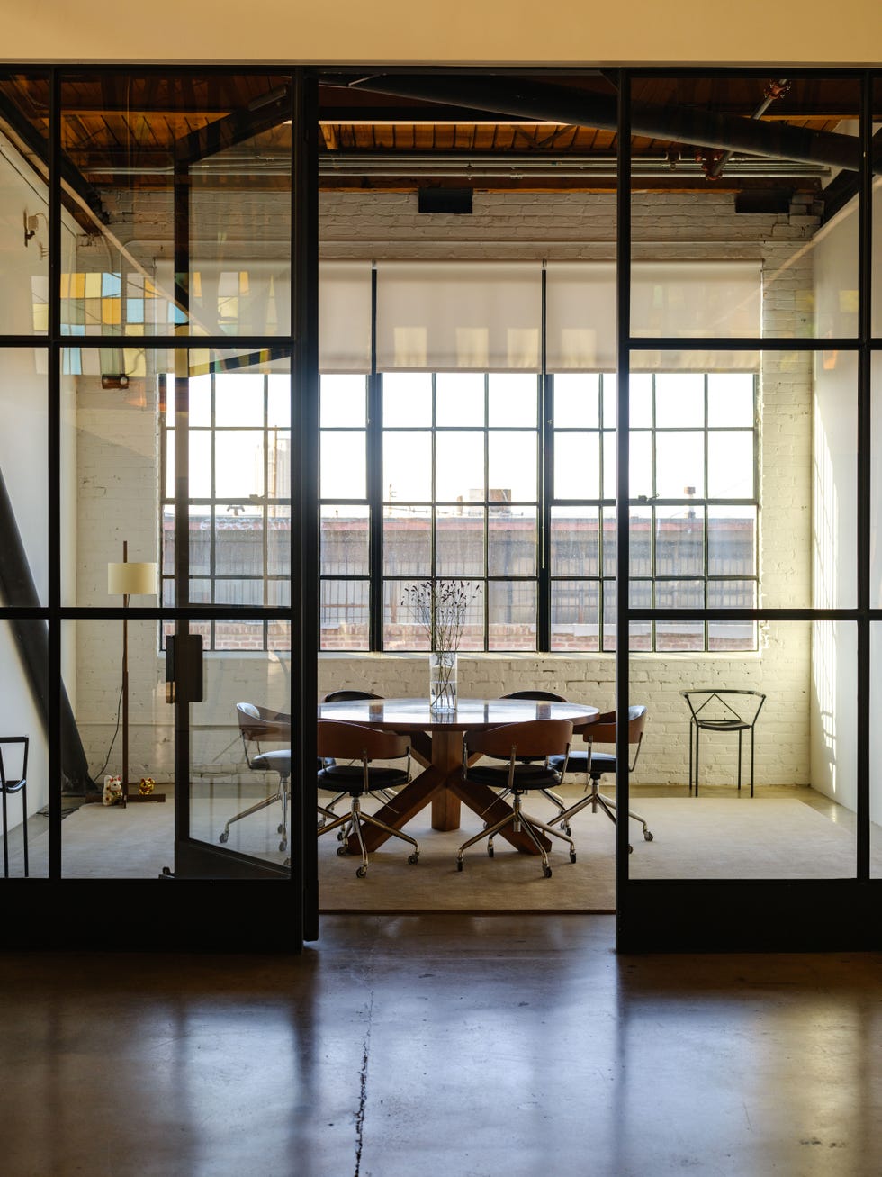 Modern conference room with a wooden table, chairs, and large windows providing natural light.