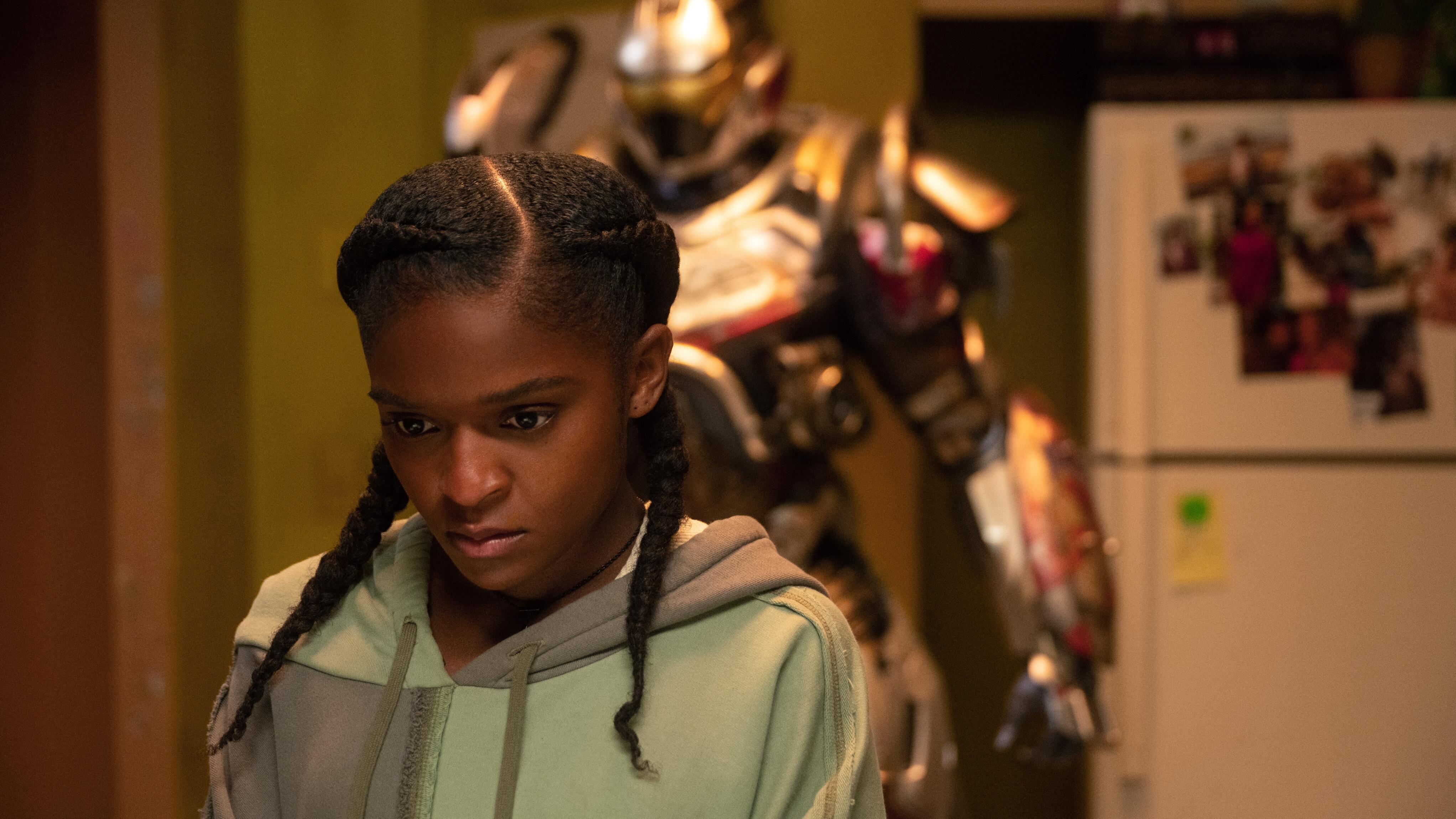 young woman stands in kitchen with robotic suit behind her