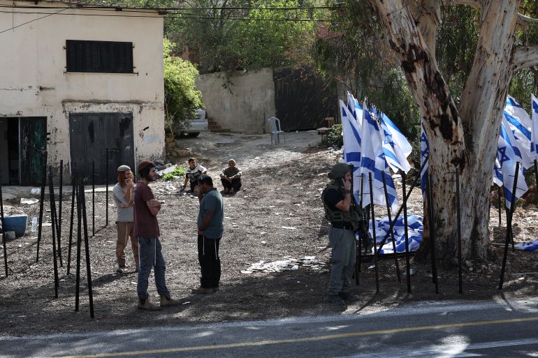 epa13289254 An Israeli security personnel member and Israeli settlers stand near Mou'ayad Mahmoud's shop in Al-Lubban Al-Sharqiya, near Nablus in the West Bank, 08 October 2026. Israeli settlers placed rows of Israeli flags outside the Palestinian-owned shop overnight, obstructing access to the business. EPA/ATEF SAFADI