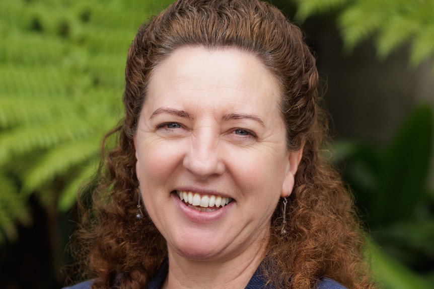 A headshot of Paula Brought smiling. She has curly brunette hair and is wearing a navy blazer and blouse.