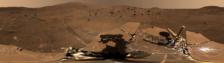 A panoramic view of a rocky, barren landscape with metallic equipment in the foreground.