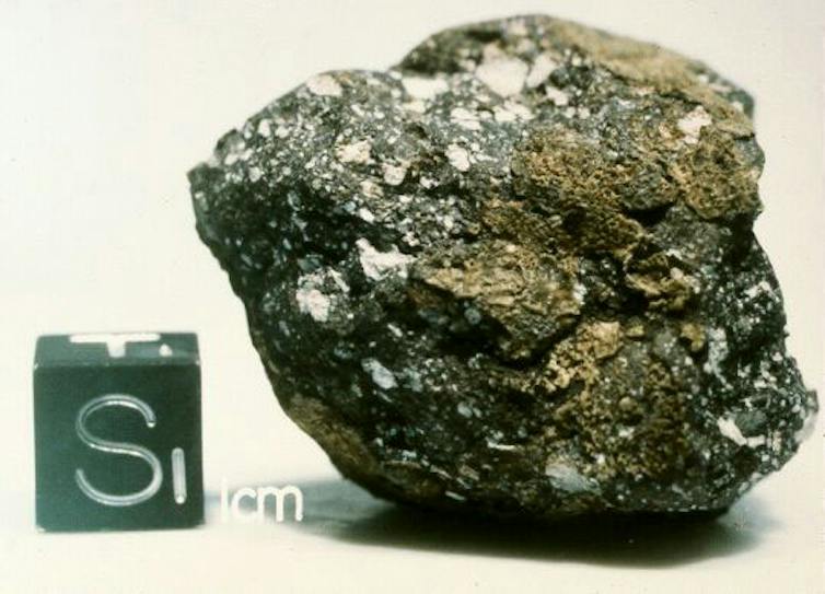 A rocky conglomerate with a 1-centimeter cube next to it for scale.