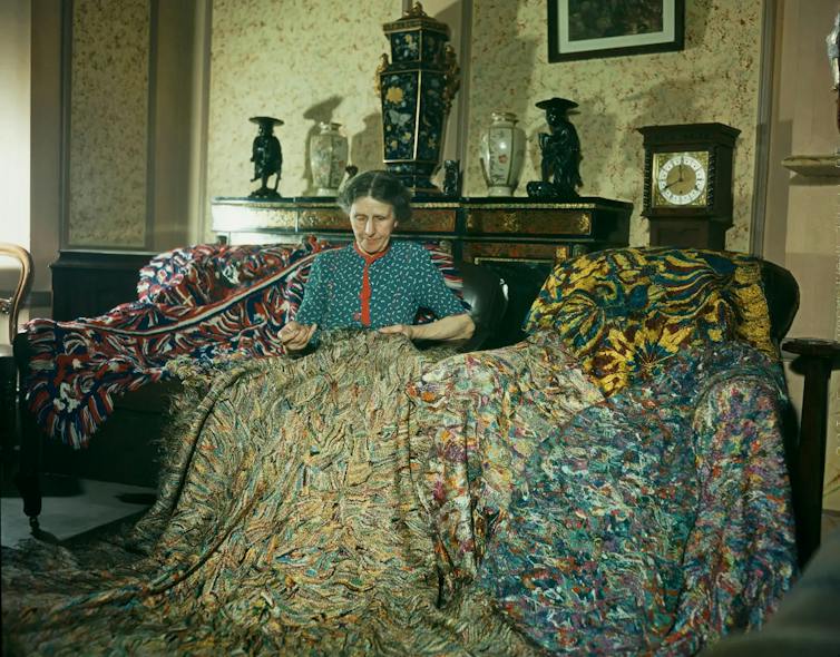 English artist Madge Gill making a rug by inserting left over strands of silk into a canvas backing.