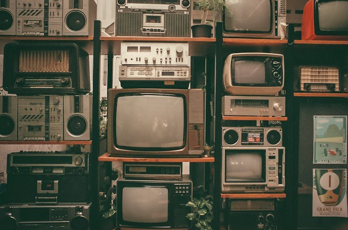 A wall shelf filled with vintage televisions and radios, an example of unique dumpster finds.
