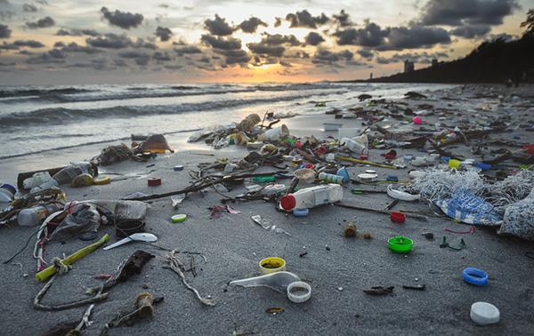 Trash and debris washed up on a beach, with the sun setting in the distance.
