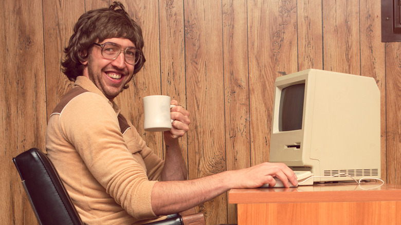 Drinking coffee at a desk with an old Apple Macintosh on it