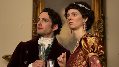 Mr Ryder (Laurie Davidson) and Caroline Bingley (Tanya Reynolds) stand in a room and hold glasses of wine. The pair look surprised by something happening offscreen. 