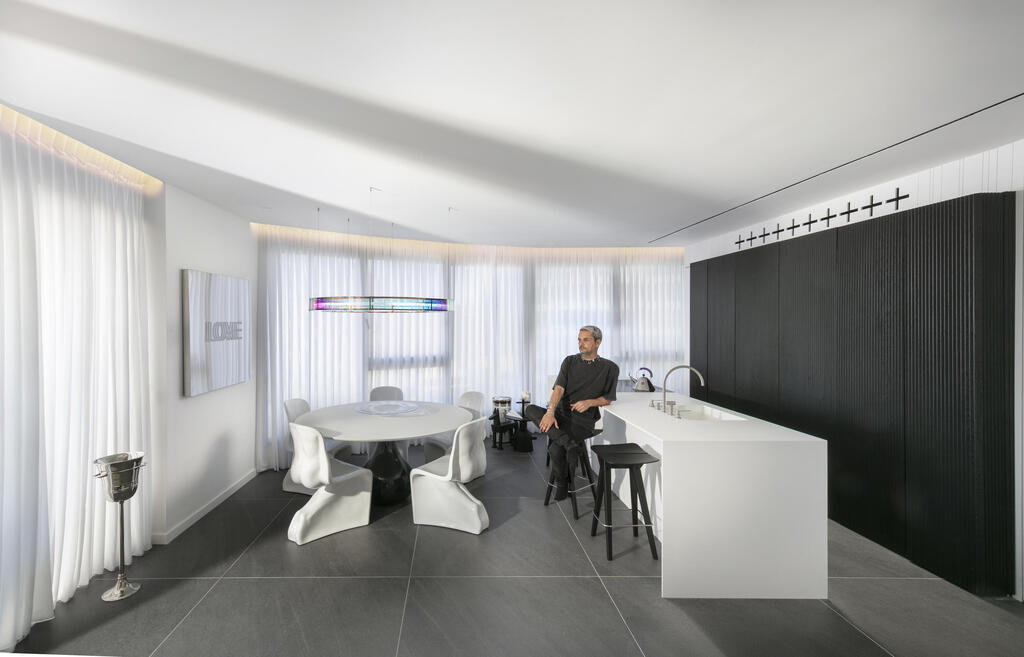 The kitchen and dining area in black and white, with the lighting fixture providing the only splash of color (Photo: Elad Gonen) דירה אולטרה מודרנית במגדל תל אביבי, עיצוב: אורון מילשטיין