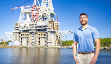 Jared Spiers, an electrical engineering technician at NASA’s Stennis Space Center, stands outdoors and poses for a portrait with the Thad Cochran Test Stand visible in the background.