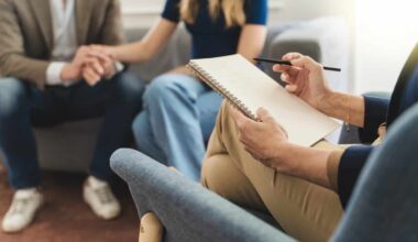 Couple therapy session: Therapist's notebook foregrounds while a young married couple holds hands in the background, seeking solutions to relationship challenges through counseling.