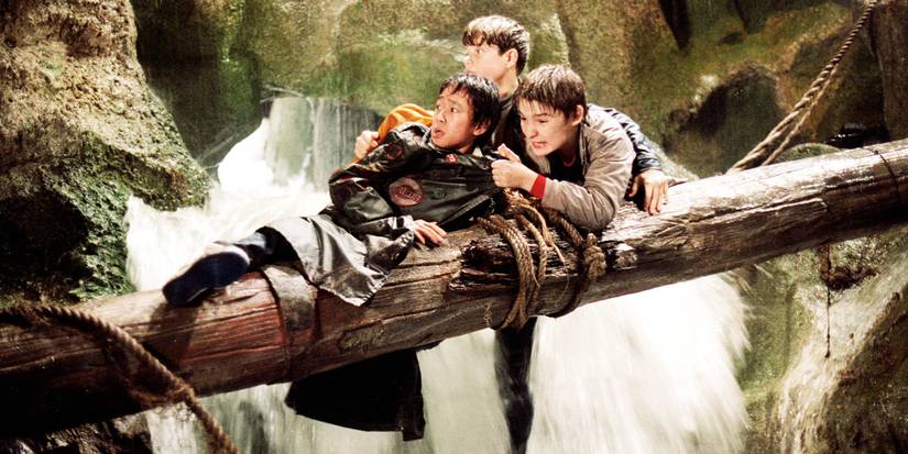 Sean Astin, Ke Huy Quan, and Corey Feldman cling to a log over a waterfall in The Goonies