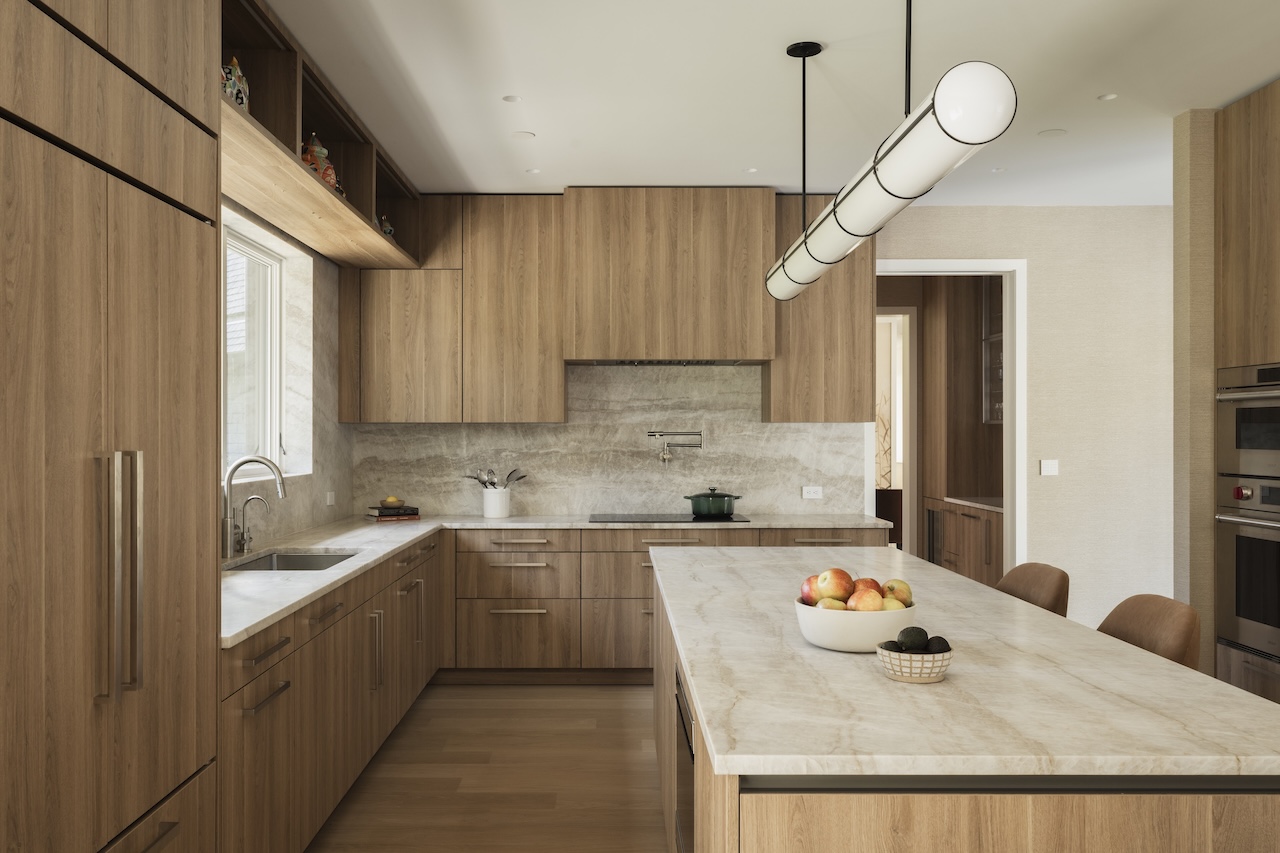 A modern kitchen with wood cabinets, stone countertops, a large island, and a cylindrical pendant light.