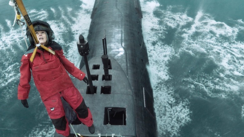 Suranne Jones as DCI Amy Silva dressed in red waterproof clothing while being lowered onto a submarine in the water by a large yellow cable.