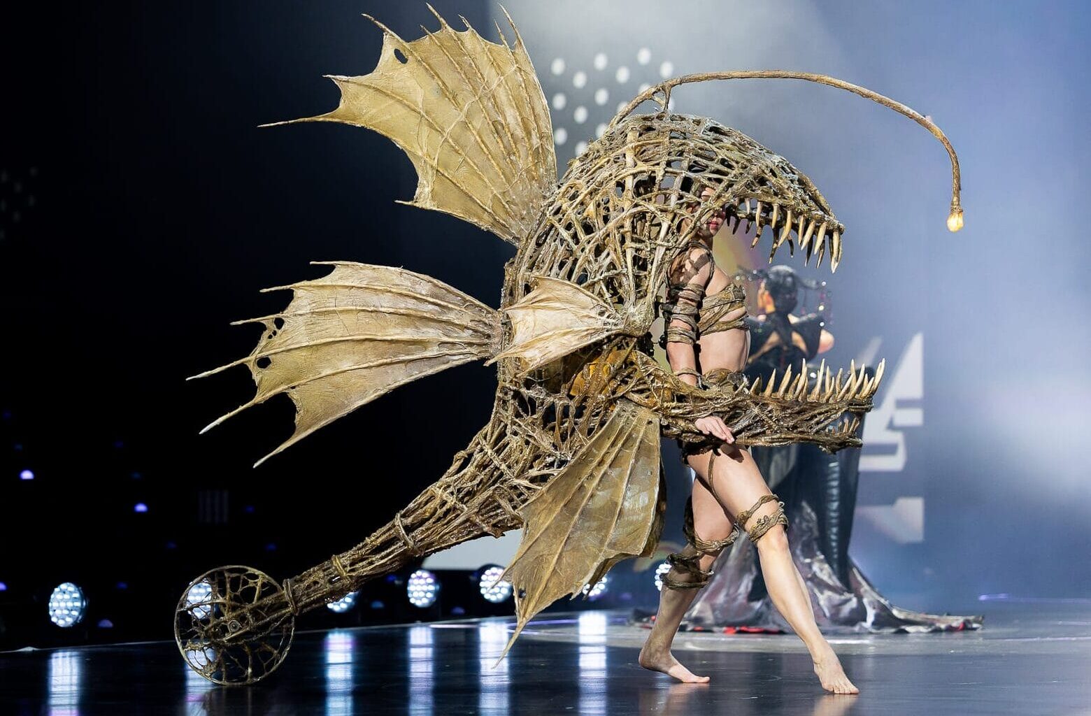 an elaborate garment being performed on stage in the form of an angler fish with its mouth over the head and torso of the wearer