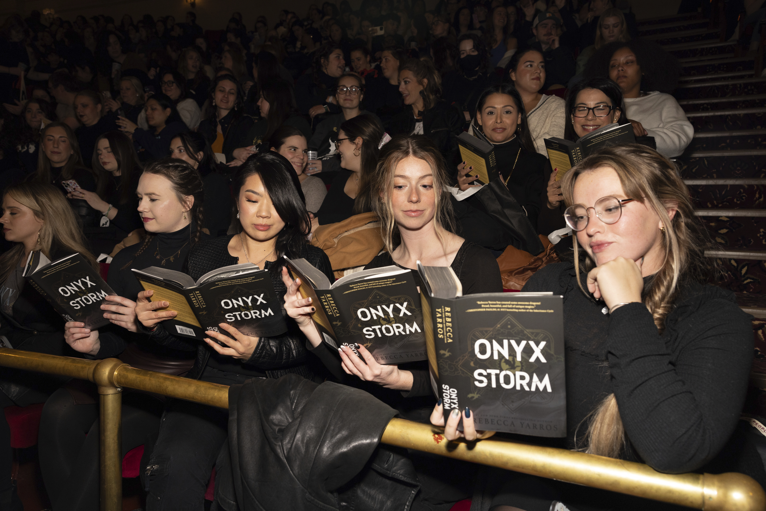 Audience members holding copies of Rebecca Yarros's *Onyx Storm* at a book event.