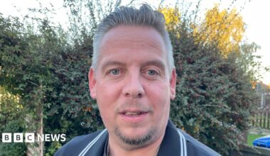 Man with goatee beard in dark shirt in front of a hedge