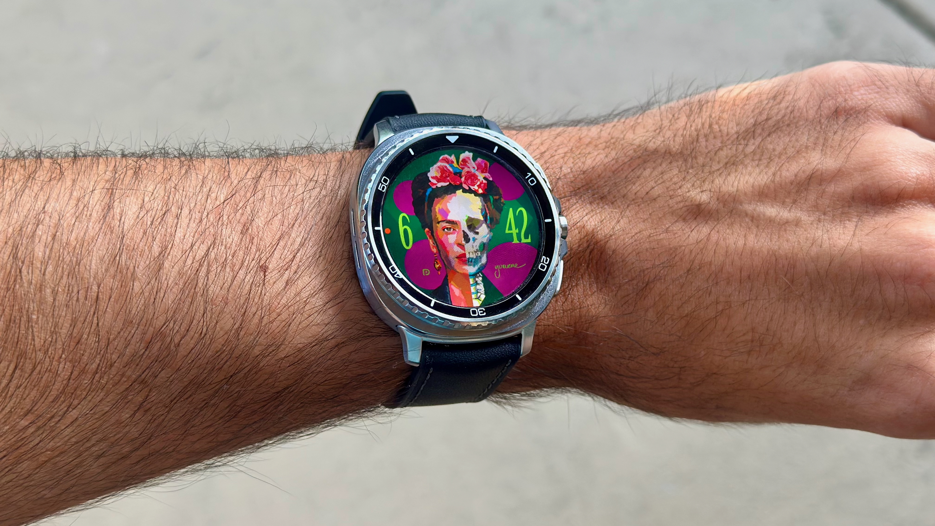 The Samsung Galaxy Watch 8 Classic on a person's wrist, showing a custom watch face from Facer with Frida Kahlo's face, half of which looks like a skeleton.