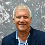 A smiling man wearing a suit in front of an abstract painting.
