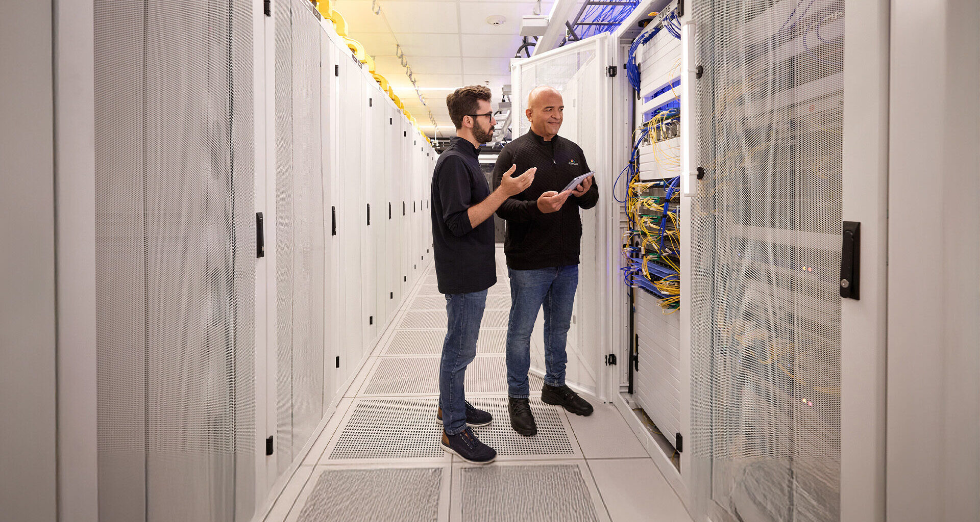 Technologists mid-conversation in a server room.