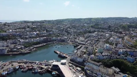 An image from above the fishing port of Brixham showing the town surrounding the harbour with boats tied up at the quay