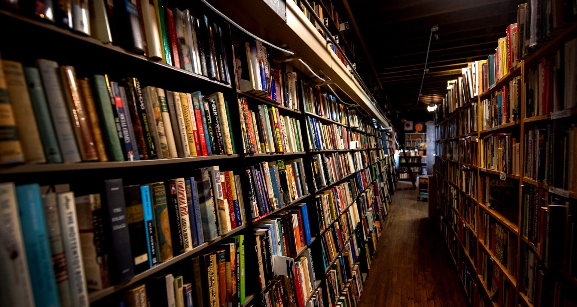 A narrow aisle lined with tall bookshelves filled with books in a dimly lit bookstore.