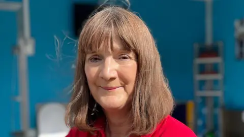 BBC A portrait picture of Flood Mary, who is wearing a red top and is smiling at the camera.