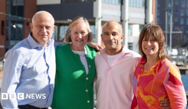 Larry Lamb at an art gallery. He has short grey hair, is wearing glasses and a green and black plaid top.