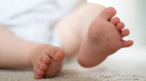 PA Media A close of photo of a baby's feet. The baby is lying on a beige carpet with his right foot slightly lifted.