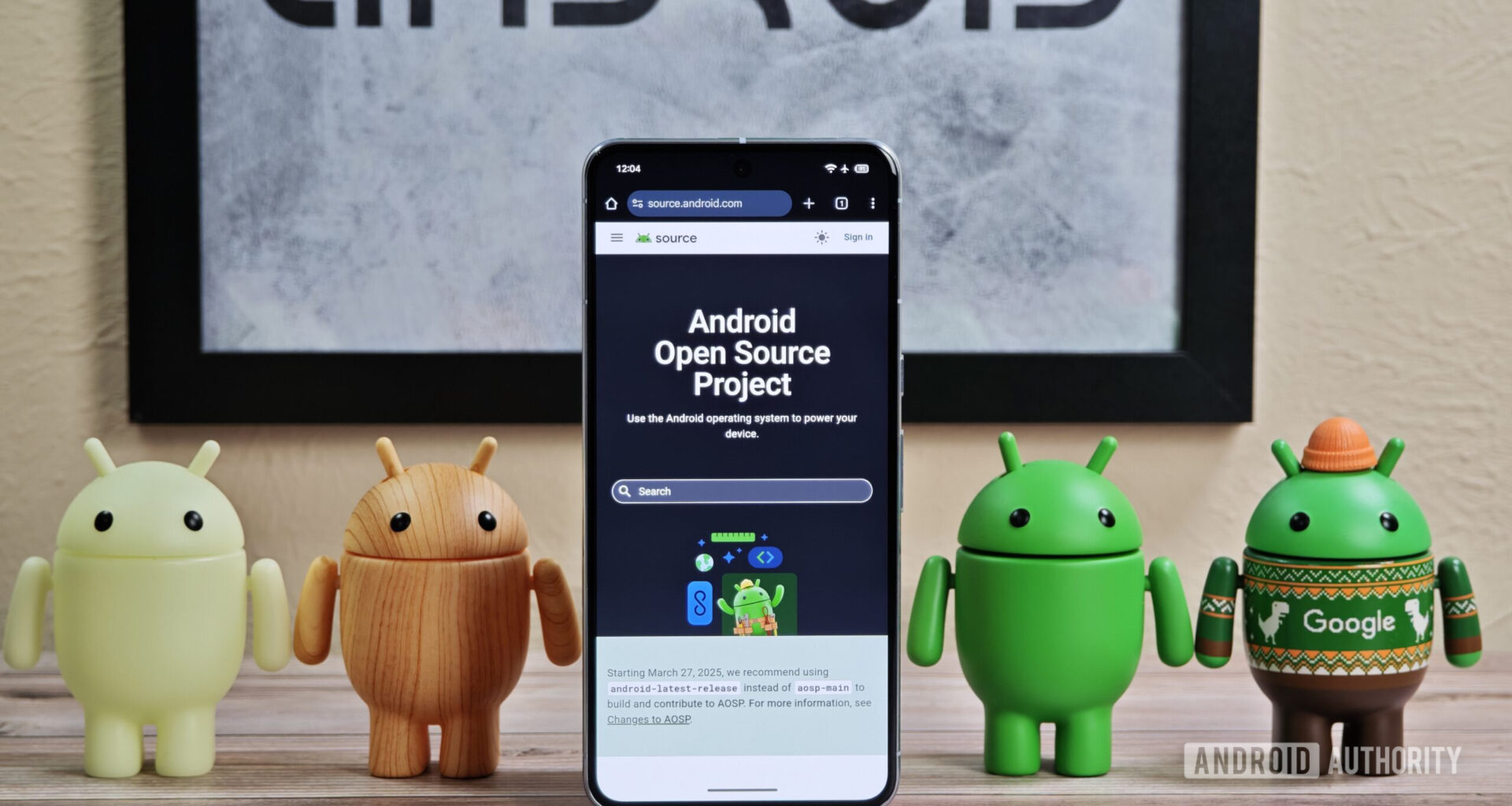 Android figures standing around Pixel phone with AOSP home page showing
