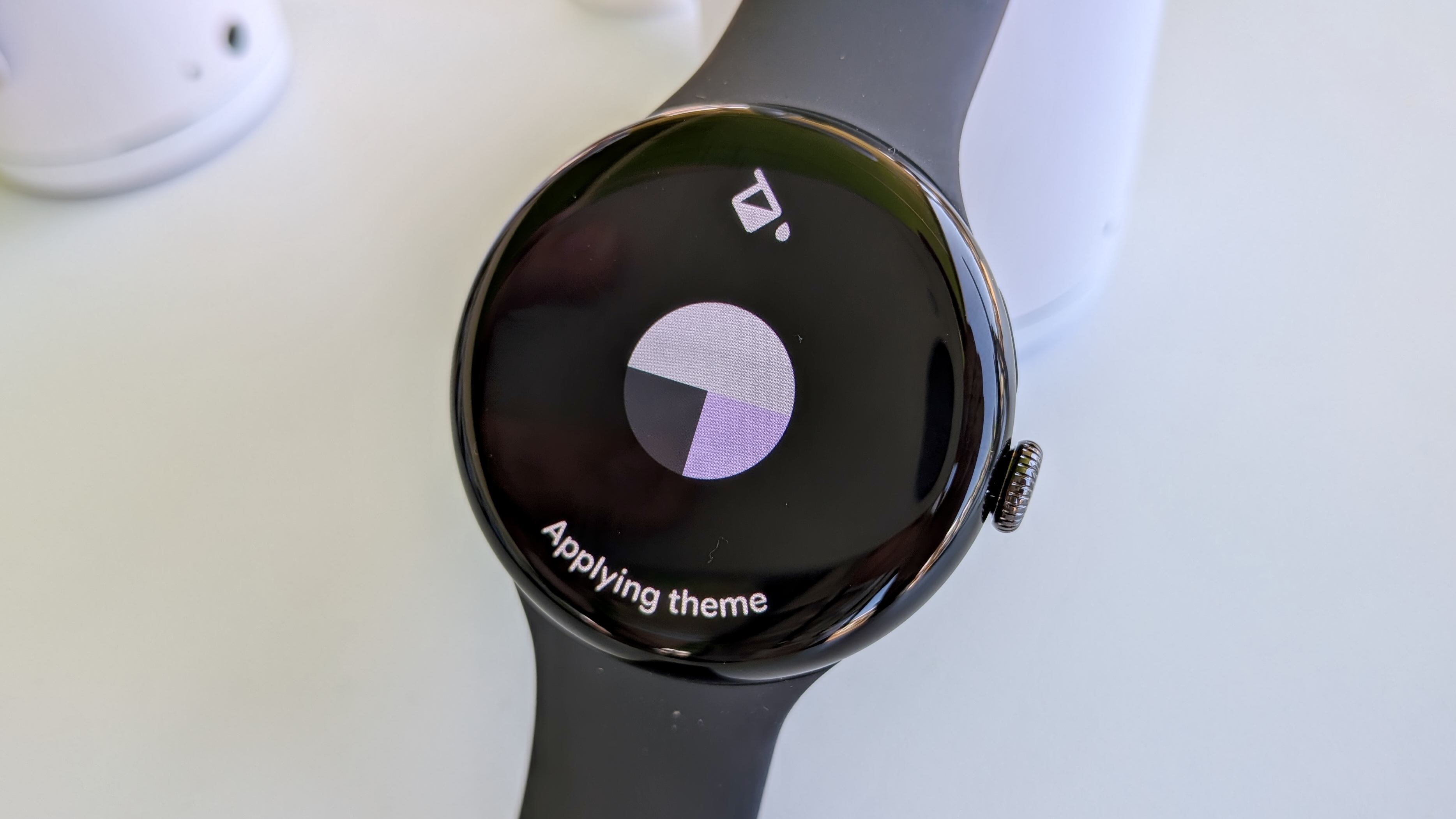 The "Applying theme" screen on Wear OS 6 on the Pixel Watch 3, showing a Paint icon above a circle showing a primary color (beige) and two secondary colors (black, pink).