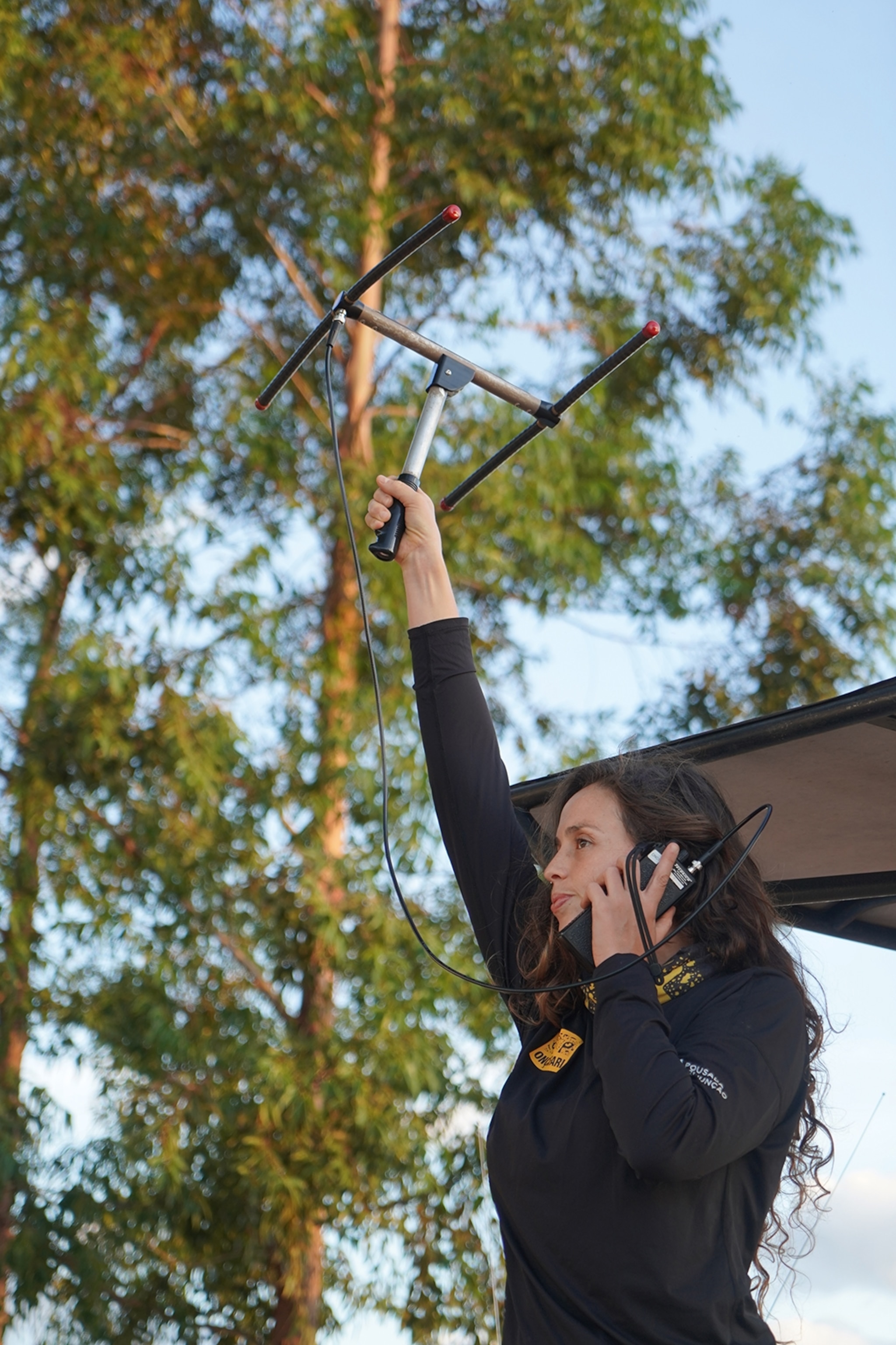 A woman holding up a VHF frequency measuring antenna, while listening to the sounds through a handheld speaker.