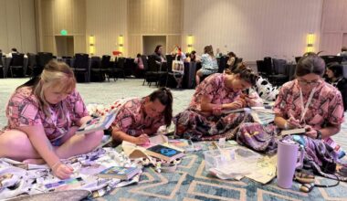 A group of friends bejewel the covers of their favorite romance novels while clad in book-themed pajamas during the Romantically Yours Convention’s pajama party event. (Hafsa Quraishi/Here & Now)