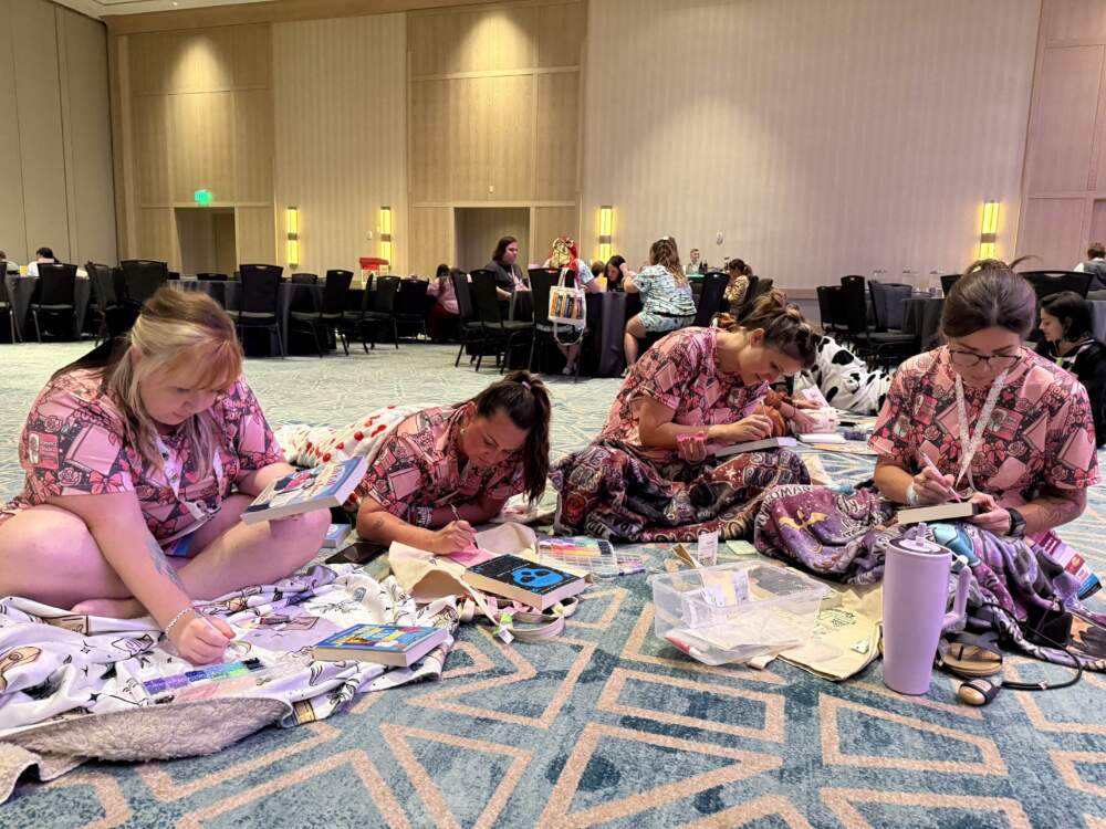 A group of friends bejewel the covers of their favorite romance novels while clad in book-themed pajamas during the Romantically Yours Convention’s pajama party event. (Hafsa Quraishi/Here & Now)