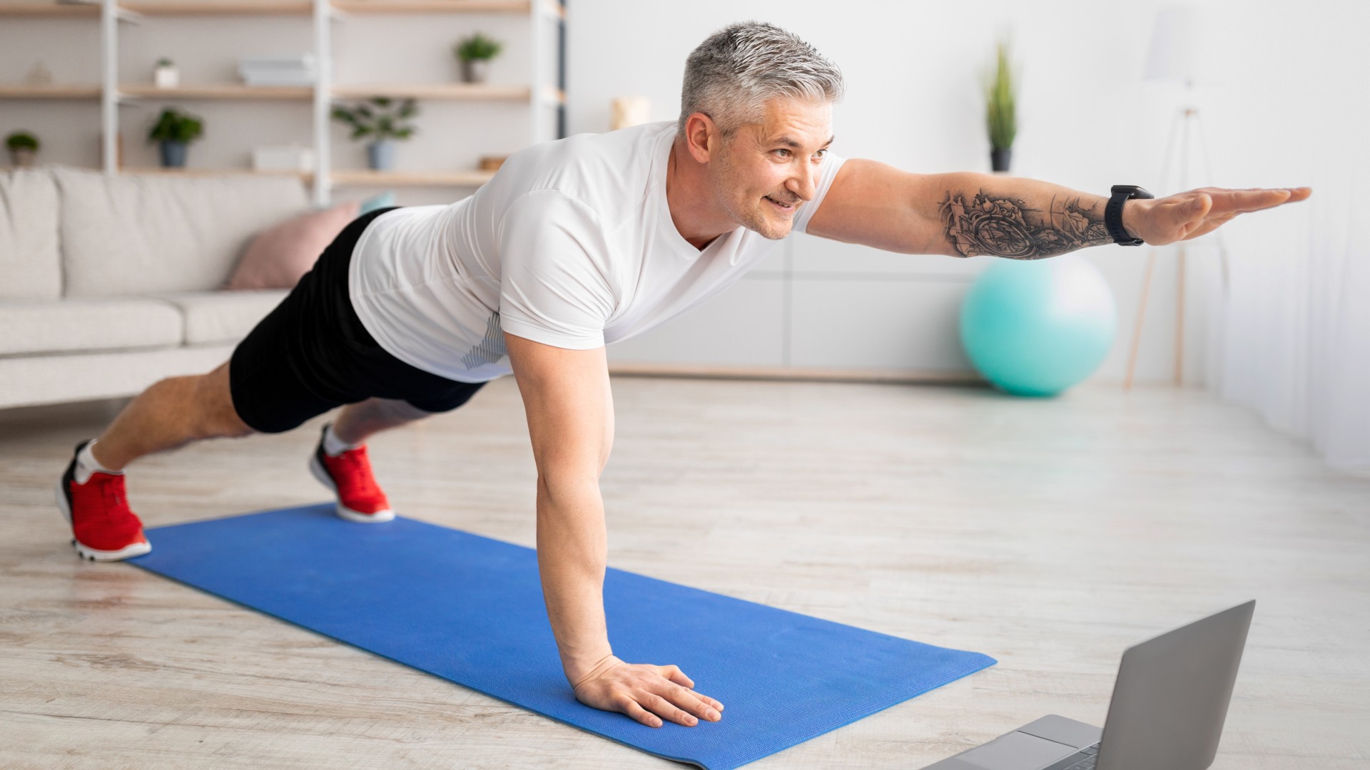 Older man performing one-arm plank on exercise mat at home during ab workout
