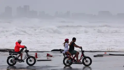 EPA Three people ride two bikes in the coast in Australia with waves crashing in the background