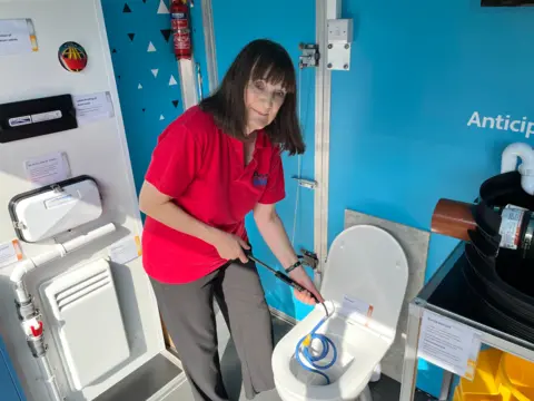 Mary demonstrating how to use the toilet pump to prevent flooding during heavy downpours.