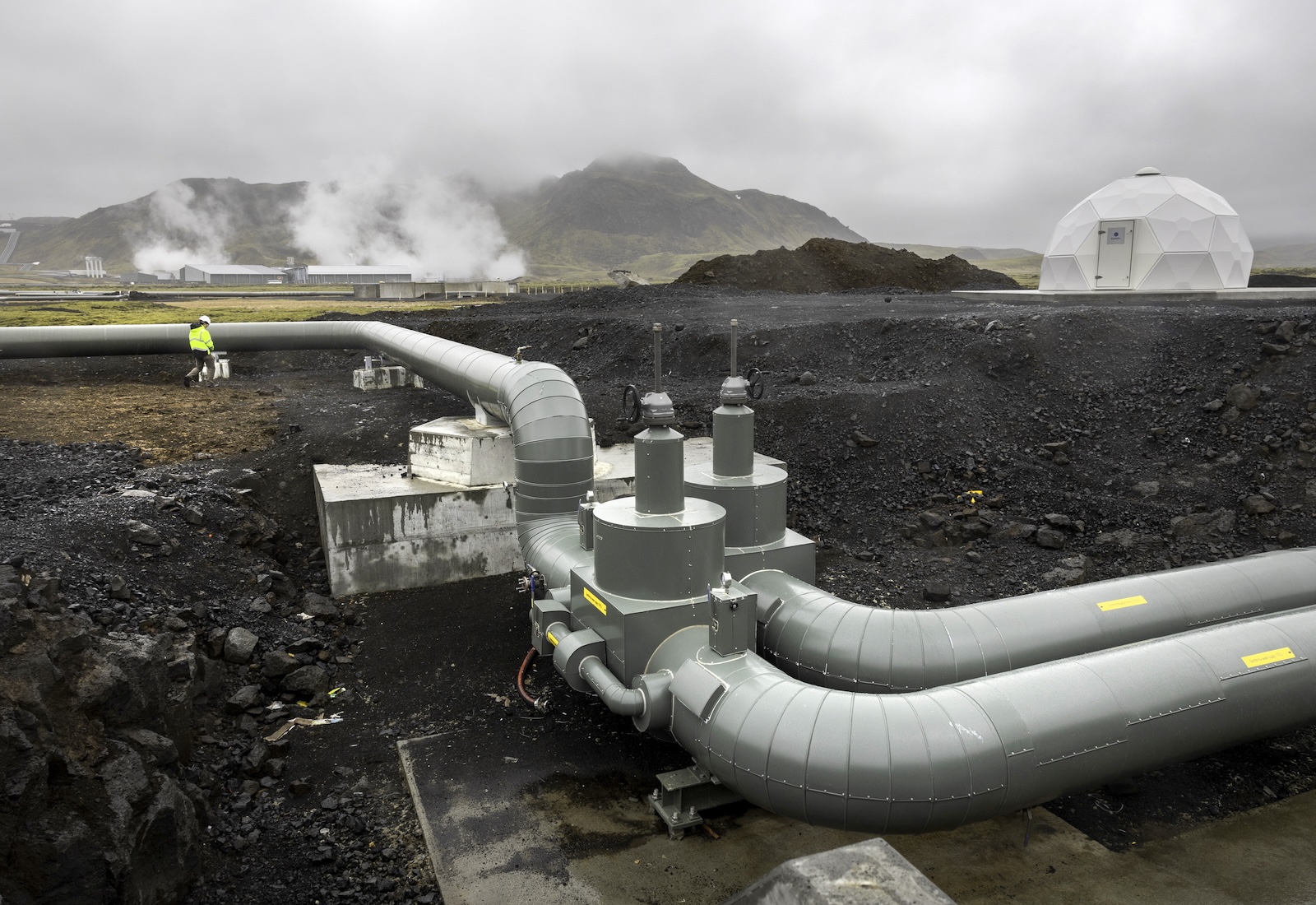Large pipes attached to an industrial facility in a rocky lansdcape, with foggy sky