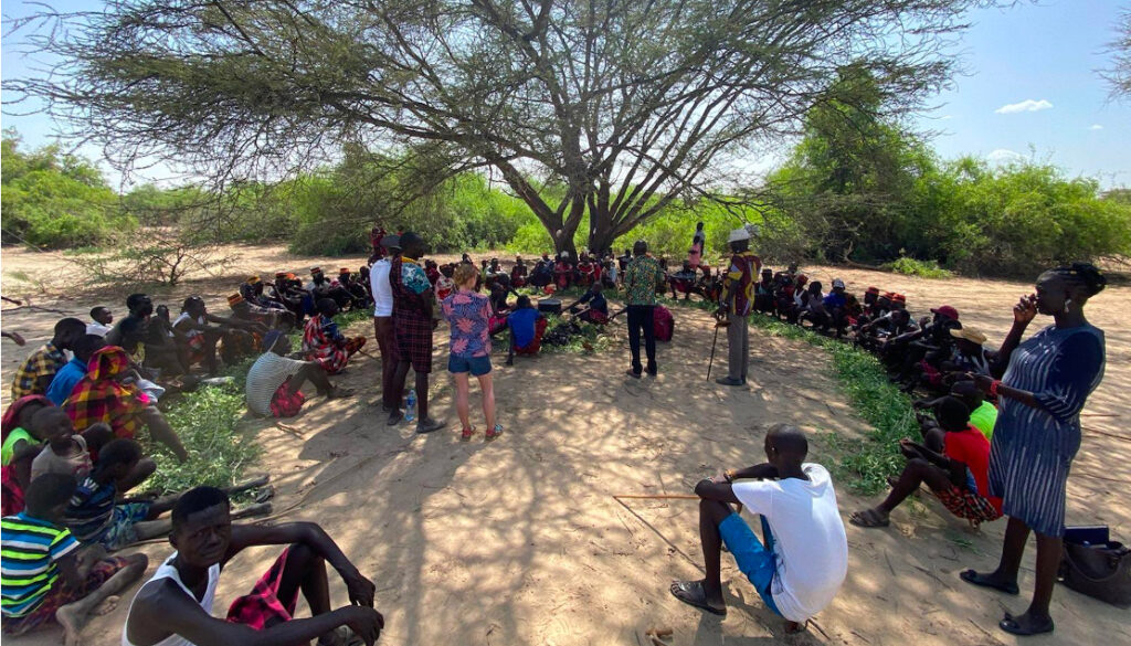 people gathered in a circle under a tree listening to standing speakers
