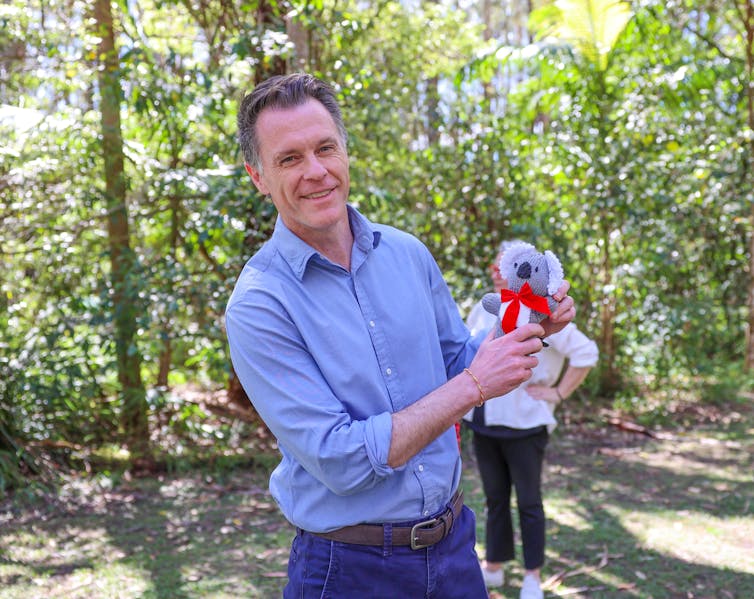 A man in a blue shirt holds a koala toy.