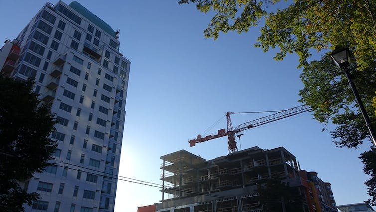a crane can be seen in the background, a high-rise apartment building in the foreground