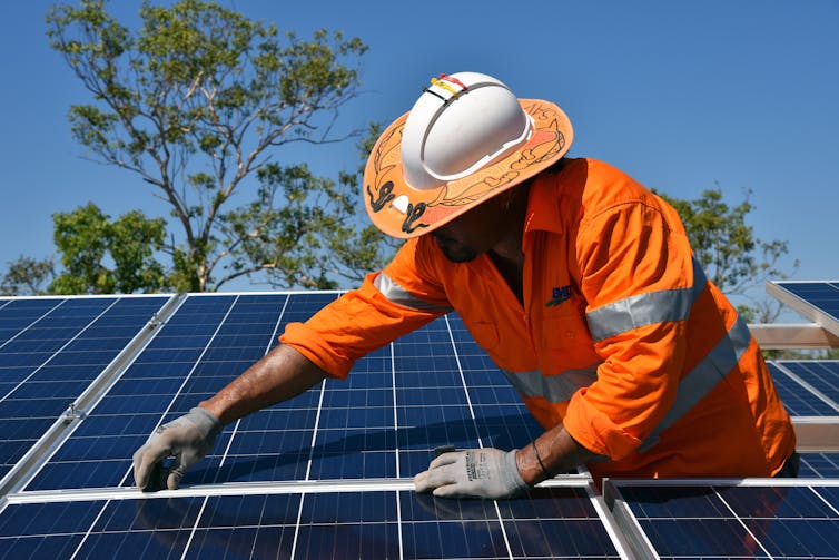 A man in orange workwear installs a solar panel.