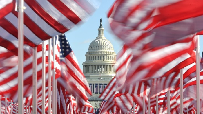 The U.S. Capitol building framed by numerous American flags on the National Mall, with the flags appearing in motion.