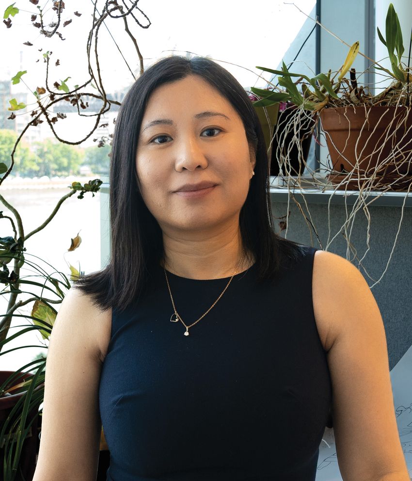Image of Li Zhao in a black top. She smiles at the camera in front of a few potted plants in the background.