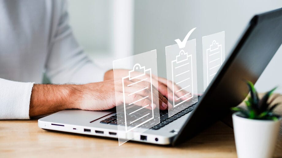 Person typing on a laptop with digital checklist icons displayed in front, one box is checked. A small plant is nearby.