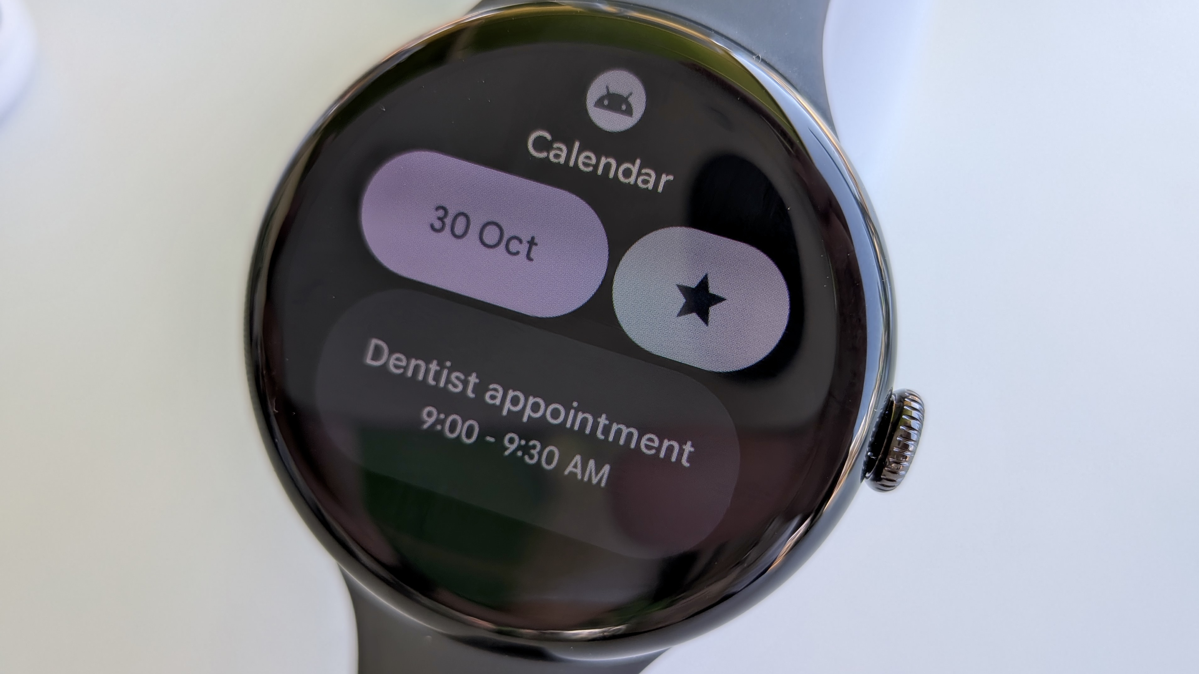 The new Calendar tile on Wear OS 6 on the Pixel Watch 3, showing the date, a Star button, and a Dentist appointment that day.