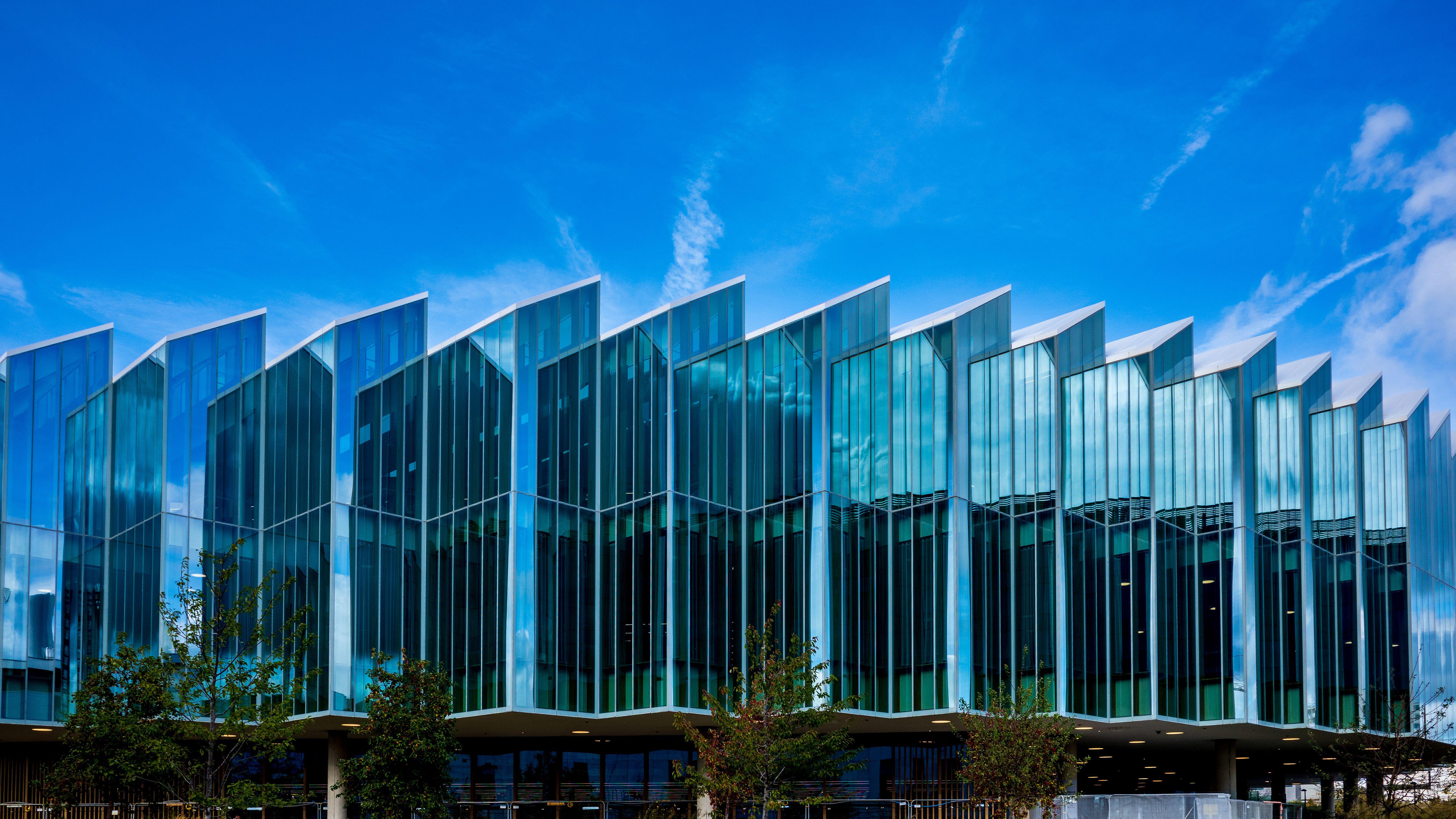 AstraZeneca Headquarters building designed by Herzog & de Meuron, featuring an angular glass facade under a bright blue sky.