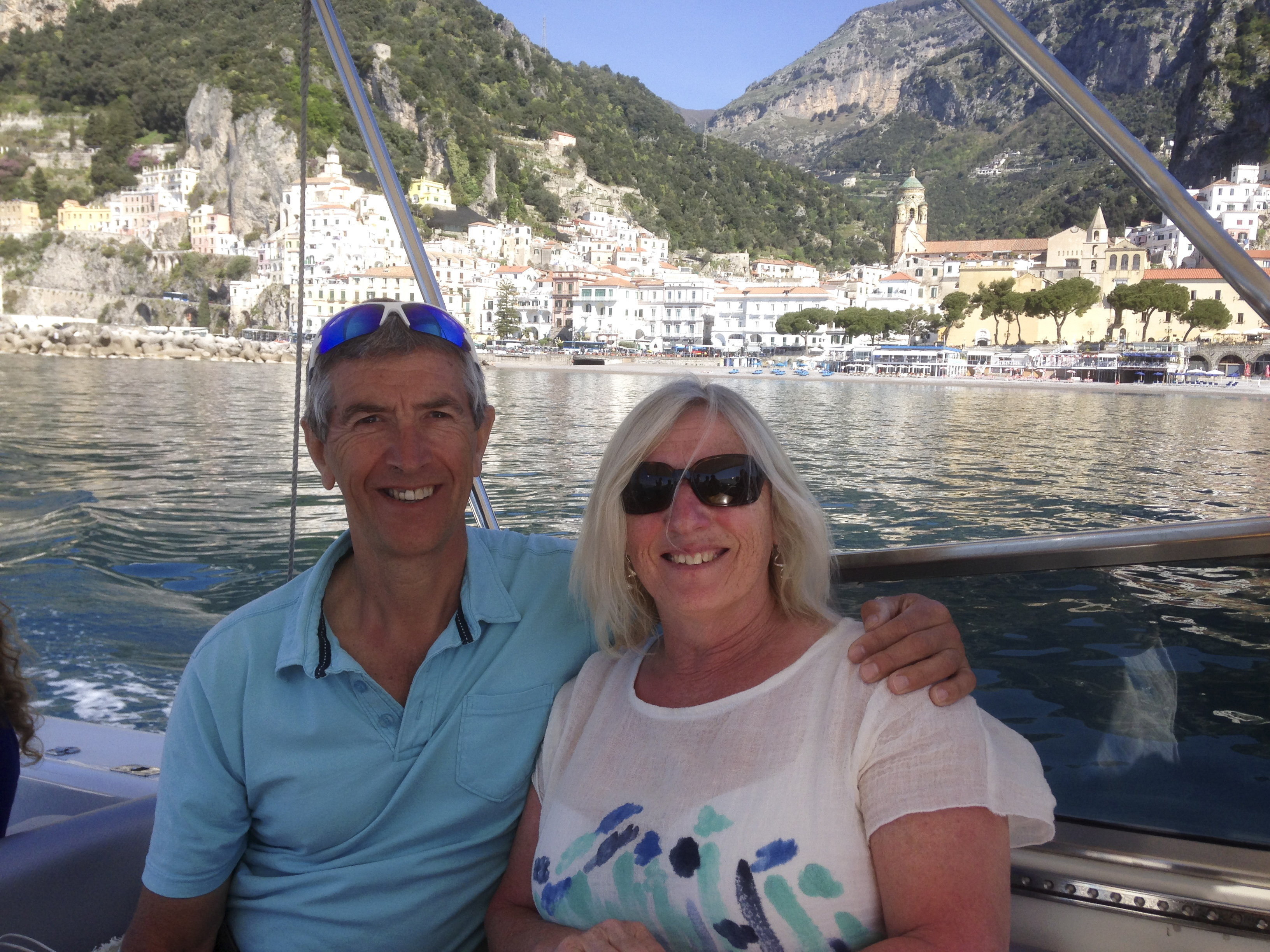 Dave and his wife before the crash, smiling on a boat with a coastal town in the background.
