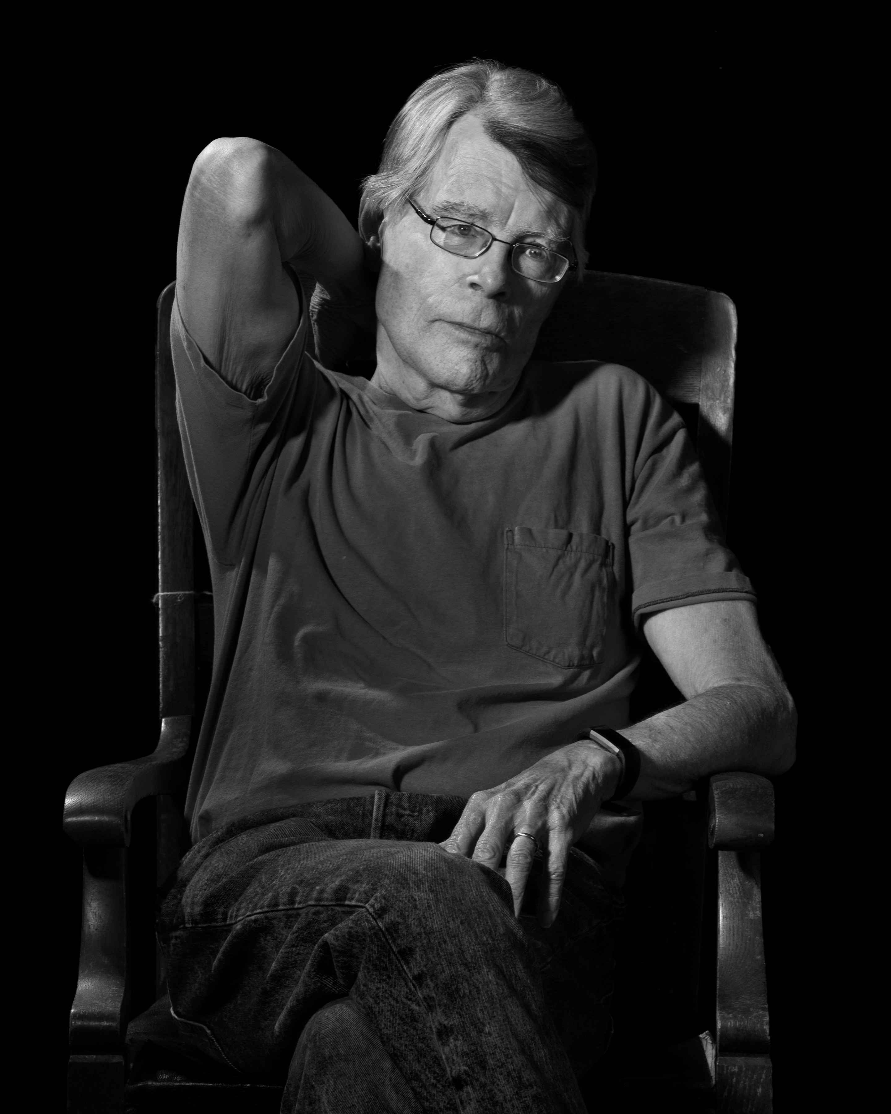 Black and white photo of Stephen King sitting in a chair.