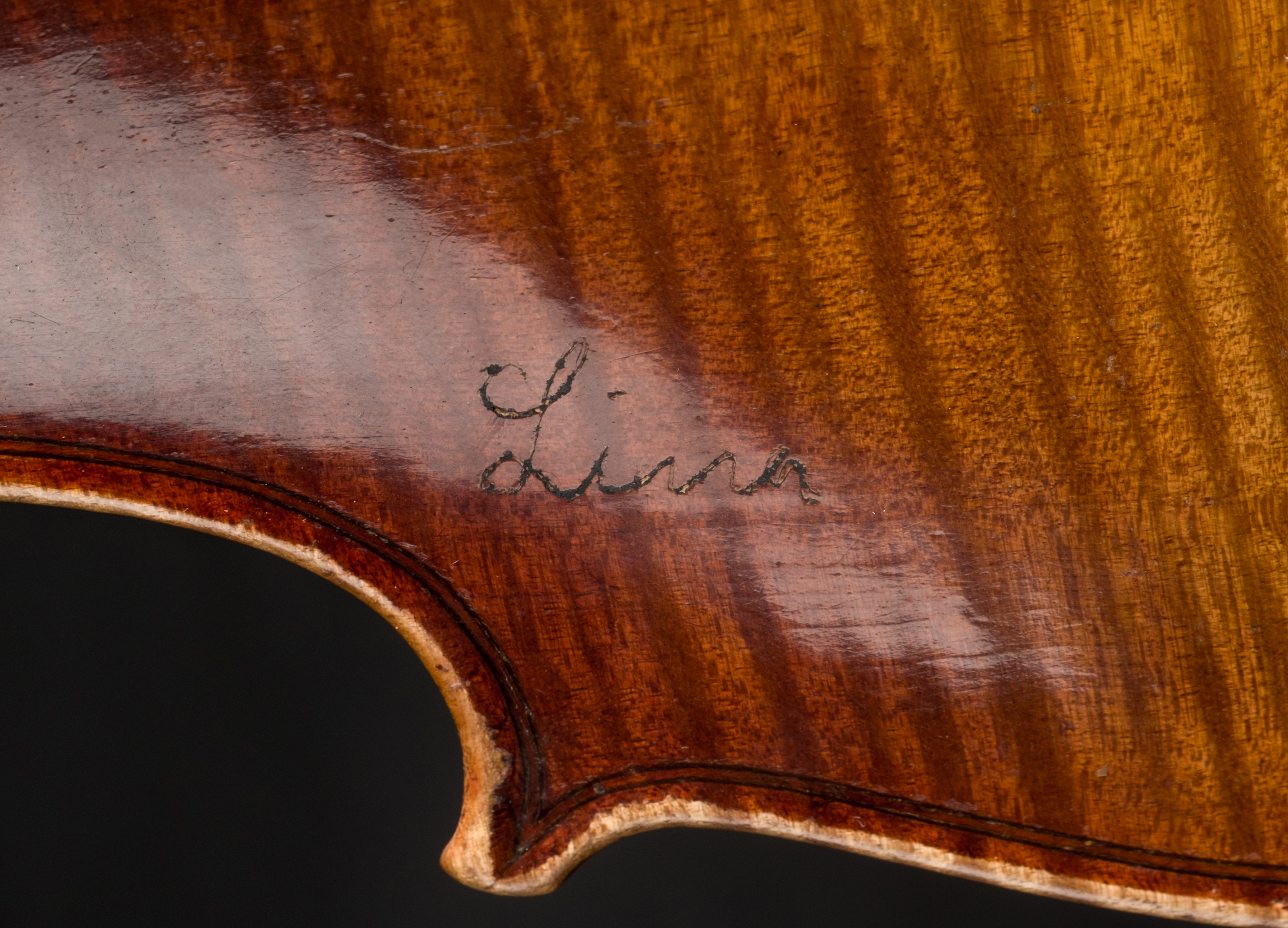 Close-up of a German violin's wooden body with the name "Lina" engraved on it.